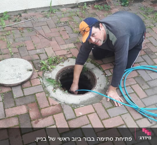 אדם עם צינור כחול בודק פתח ביוב